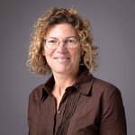 Das lvh-Team Porträt einer Frau mit lockigen Haaren und Brille vor grauem Hintergrund