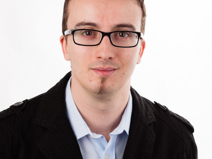 Zufrieden – trotz schwieriger Zeiten! Porträt eines jungen Mannes mit Brille und schwarzer Jacke vor weißem Hintergrund