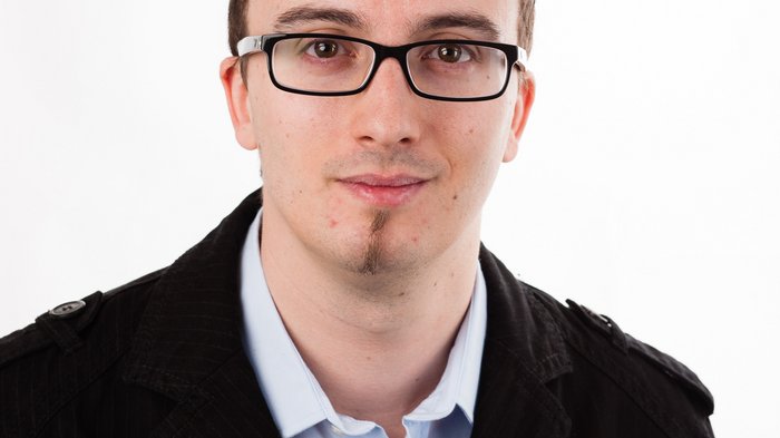 Zufrieden – trotz schwieriger Zeiten! Porträt eines jungen Mannes mit Brille und schwarzer Jacke vor weißem Hintergrund