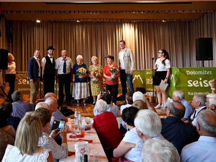 Gli Artigiani Anziani si sono incontrati a Siusi allo Sciliar Persone a un evento comunitario con fiori e oratrice sul palco