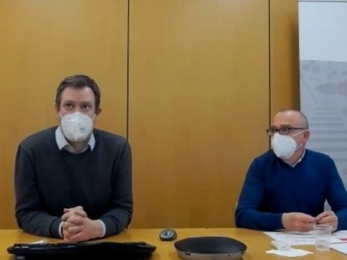 AHA und konsequentes Testen, bis sich die Situation entspannt Zwei Männer mit Masken bei einer Besprechung an einem Tisch