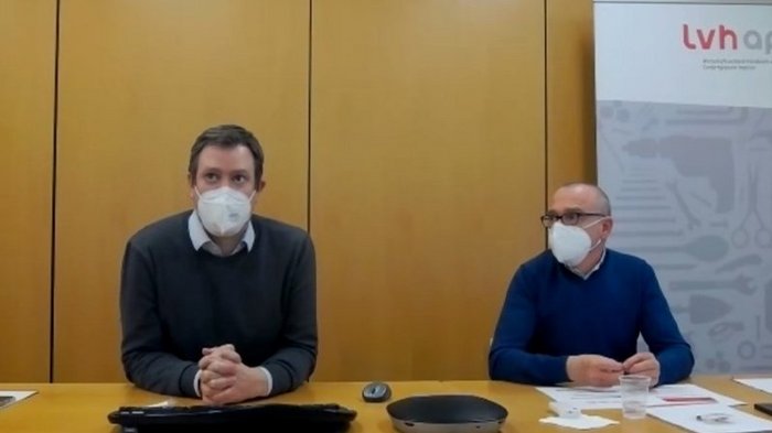 AHA und konsequentes Testen, bis sich die Situation entspannt Zwei Männer mit Masken bei einer Besprechung an einem Tisch