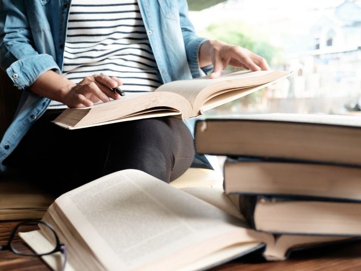Weiterbildung Person liest und macht Notizen in einem großen Buch umgeben von mehreren Büchern