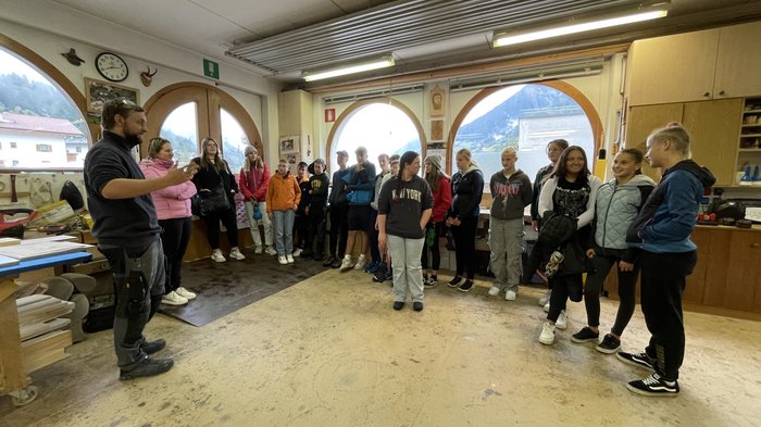 Berufsinformationskampagne St. Leonhard im Passeier Gruppe Jugendlicher in Werkstatt, hört einem Mann zu, der vorne spricht
