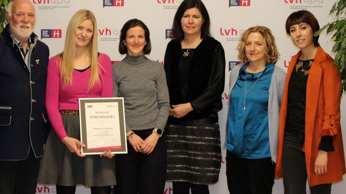 Come dare valore ai vestiti Sei persone durante una premiazione con attestato davanti allo sfondo LVH-Apo