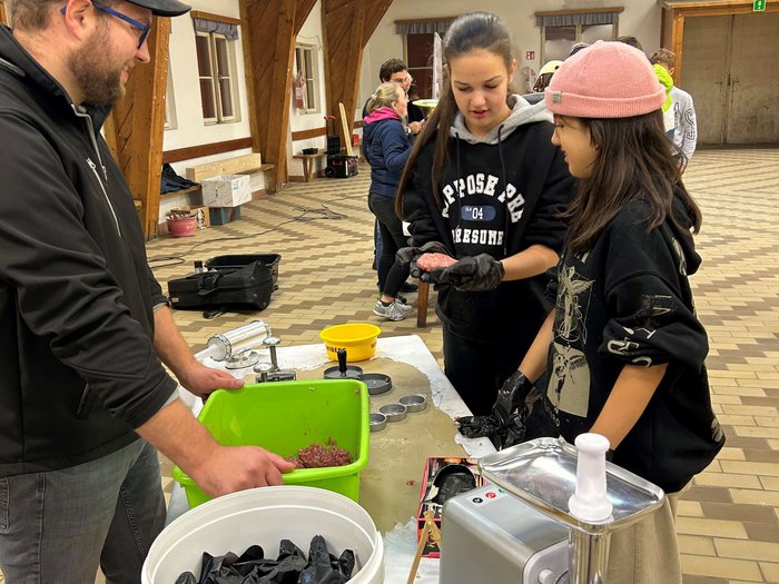 JHW-Wipptal Personen formen Hackfleisch in einer Halle mit Fleischwolf auf dem Tisch