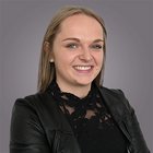 Greta Kienzl Ritratto di giovane donna sorridente con camicetta di pizzo nera e giacca di pelle su sfondo grigio