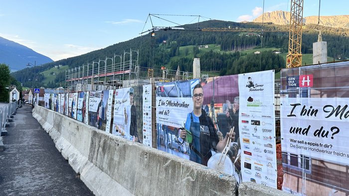 Jugend motivieren! Bauzaun mit Bannern und Plakaten vor einer Baustelle in den Bergen