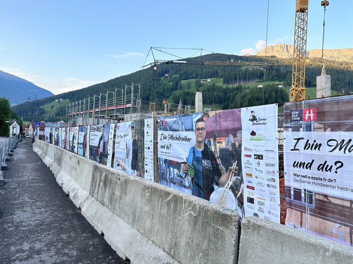Jugend motivieren! Bauzaun mit Bannern und Plakaten vor einer Baustelle in den Bergen