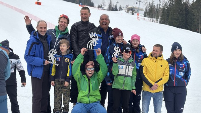 Handwerker/innen tauschen Werkzeuge gegen Skier und Rodel Gruppenfoto mit Skiteam und Gewinnern auf Siegerpodest im Schnee