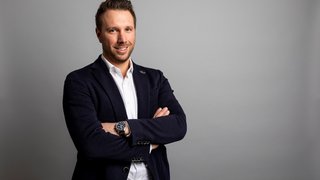 News Junger Mann in Anzugjacke vor grauem Hintergrund mit verschränkten Armen