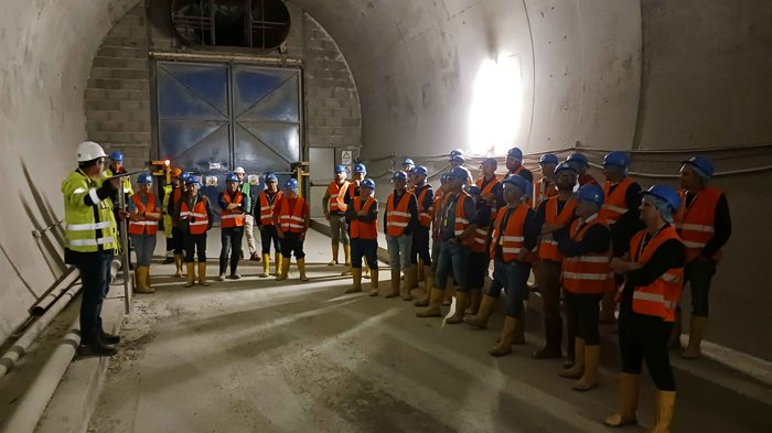Fachlicher Austausch im Zeichen eines Jahrhundertprojekts Gruppe Bauarbeiter mit Schutzhelmen und Warnwesten in Tunnel mit Anleitung