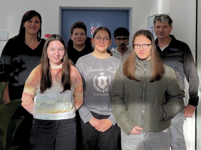 Mittelschule Gossensaß: Berufe praxisnah erleben Gruppe von sieben Personen steht vor einer blauen Tür in einem hellen Raum