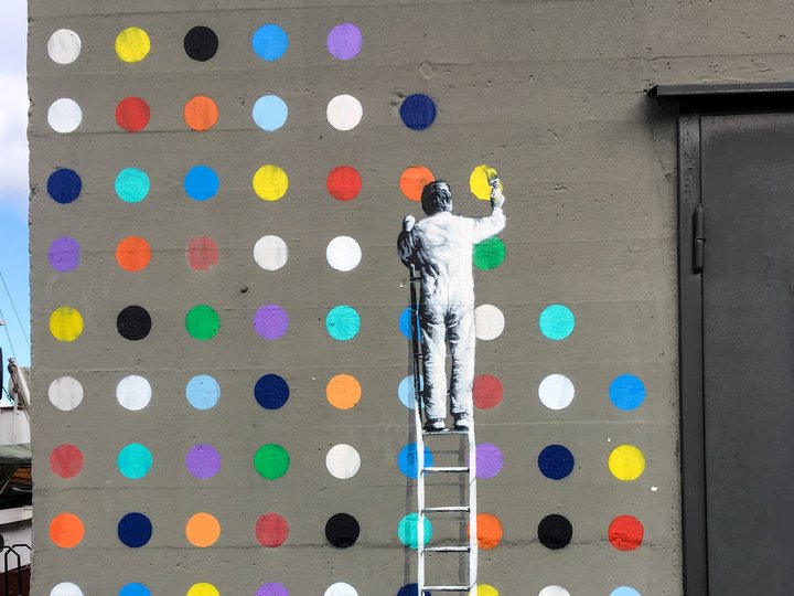 Incentivi innovativi e allo sviluppo di prodotti Murale di un uomo su una scala che dipinge punti colorati su un muro grigio