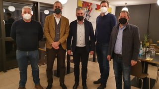 News Fünf Männer mit Masken stehen in einem Raum mit Tischen und Lampen