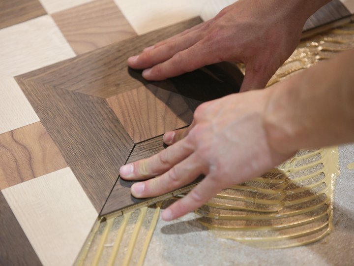 Percorso formativo Mani che posano parquet in legno sul pavimento con adesivo