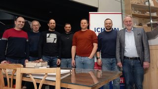 News Sieben Männer stehen nebeneinander vor einem Tisch und einem Werbebanner