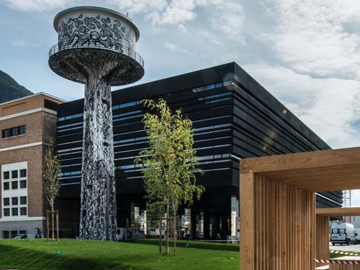 Was passiert im Maker Space? Wasserturm mit Graffiti in einem modernen Stadtpark neben Holzmöbeln