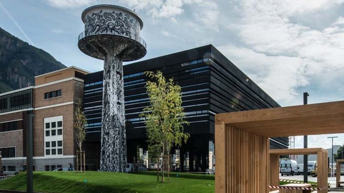 Was passiert im Maker Space? Wasserturm mit Graffiti in einem modernen Stadtpark neben Holzmöbeln