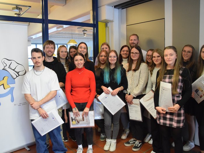 Feierlicher Abschluss im BBZ „Emma Hellenstainer“: Neue Fachkräfte im Konditor-, Bäcker- und Metzgerhandwerk ausgezeichnet Gruppe junger Menschen hält Zertifikate bei einer Abschlussfeier in Innenräumen