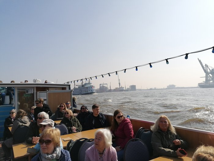Die Althandwerker besuchen Hamburg Menschen sitzen auf einem Boot und fahren auf einem Fluss mit Industriehafen im Hintergrund