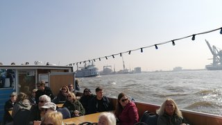 News Menschen sitzen auf einem Boot und fahren auf einem Fluss mit Industriehafen im Hintergrund