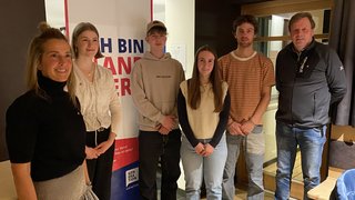 News Sechs Menschen stehen vor einem Ich bin Handwerker Banner im Innenraum