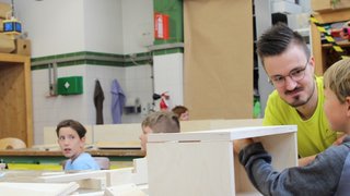 News Lehrer unterstützt Kinder beim Holzarbeiten in einer Werkstatt