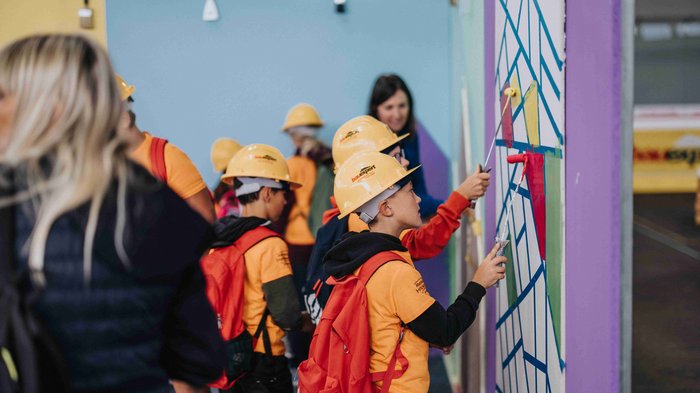 "Abenteuer Handwerk" - Initiative begeistert junge Generation für Handwerksberufe im Pustertal Kinder mit Bauhelmen malen eine Wand während einer Gruppenaktivität
