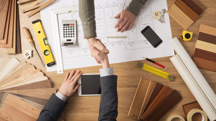 Öffentliche Aufträge – ein wichtiger Halt in der Krise Zwei Personen schütteln sich über einem Architekturplan die Hände