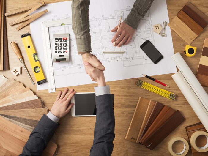 Öffentliche Aufträge – ein wichtiger Halt in der Krise Zwei Personen schütteln sich über einem Architekturplan die Hände