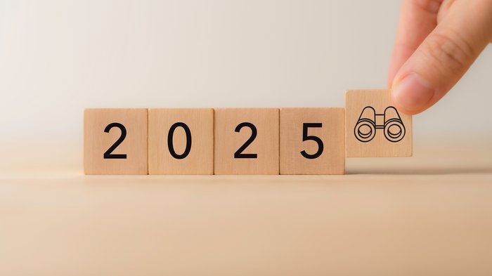 Barometro dell’economia IRE – Primavera 2025 Dopo un modesto 2024, la manifattura guarda con fiducia al 2025 Mano posiziona cubo con binocolo accanto ai numeri 2025 su tavolo di legno