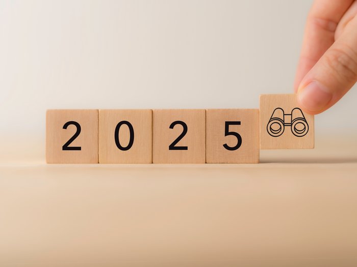 WIFO-Wirtschaftsbarometer Frühjahr 2025: Nach einem bescheidenen 2024 blickt das Verarbeitende Gewerbe zuversichtlich auf 2025 Hand setzt Würfel mit Fernglas neben Zahlen 2025 auf Holztisch