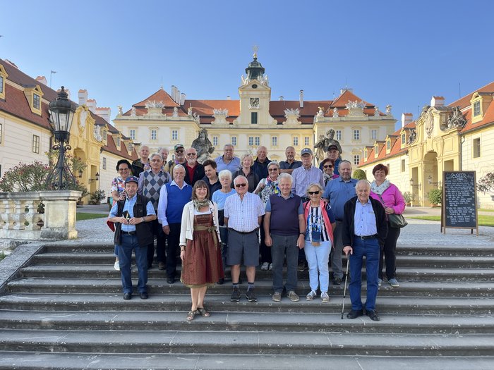 Althandwerker/innen unterwegs: Rundfahrt Weinviertel Gruppe älterer Menschen auf Treppen vor einem historischen Schloss bei sonnigem Wetter