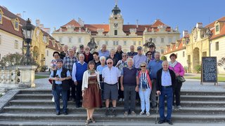 News Gruppe älterer Menschen auf Treppen vor einem historischen Schloss bei sonnigem Wetter