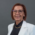 Media Ritratto di donna con occhiali, blazer bianco e capelli rossi corti su sfondo grigio