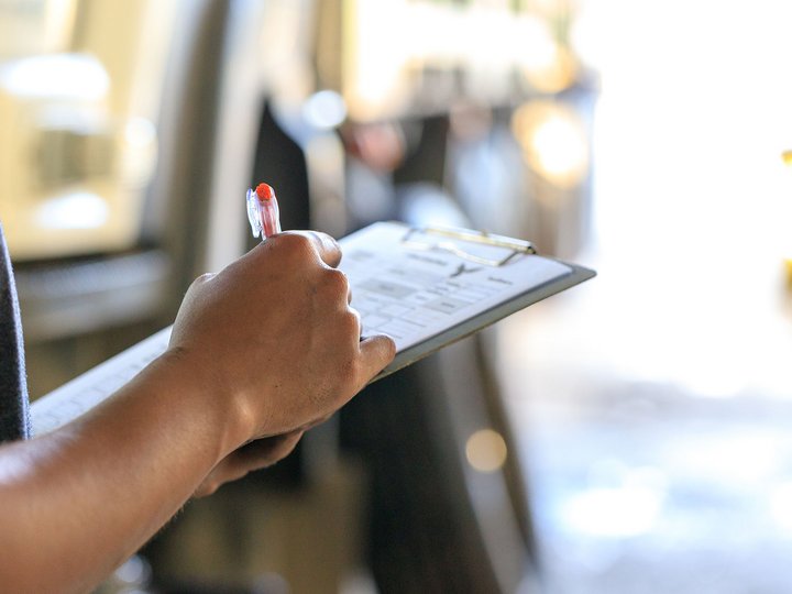 Komkrich Marom/ Shutterstock.com Person hält Klemmbrett und schreibt mit rotem Stift