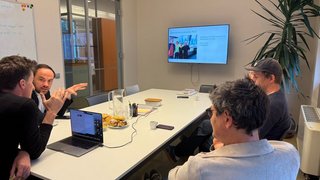 News Vier Personen bei einer Besprechung in einem Konferenzraum mit Laptop und Bildschirm