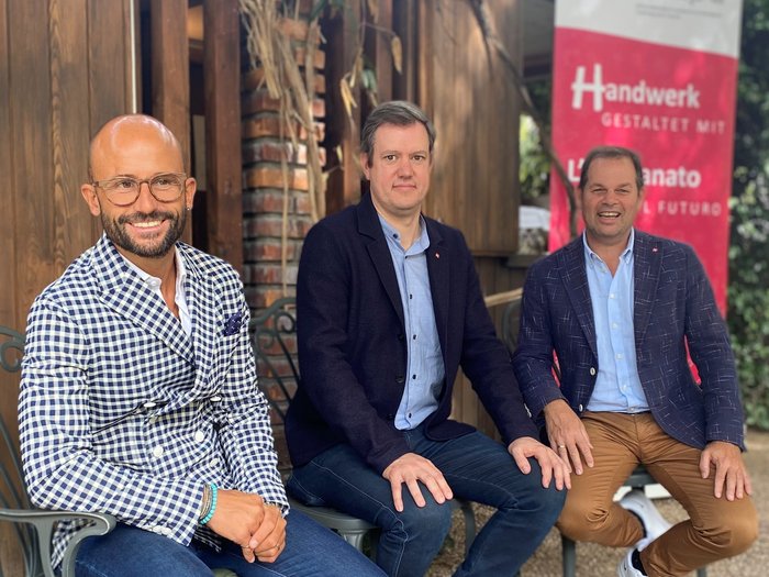 L'artigianato ha bisogno di leggi chiare e procedure snelle Tre uomini seduti davanti a una casa di legno con striscione su artigianato e futuro