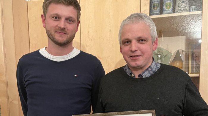 Handwerk Margreid wählt neuen Ausschuss Zwei Männer halten ein gerahmtes Foto einer Gruppe Personen in einem Wohnraum