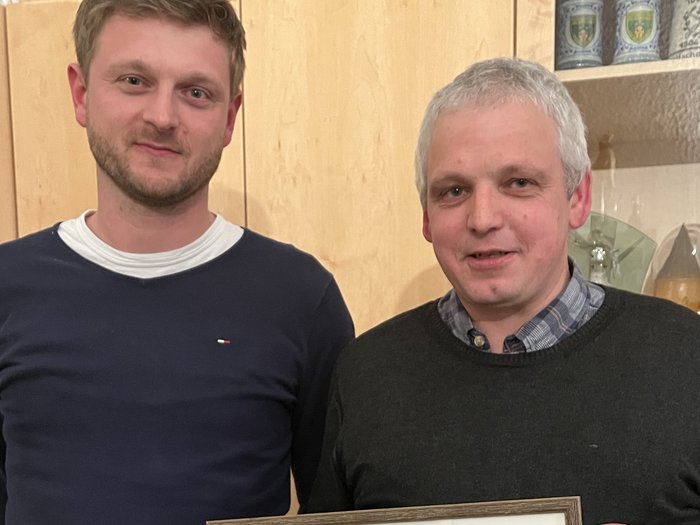 Handwerk Margreid wählt neuen Ausschuss Zwei Männer halten ein gerahmtes Foto einer Gruppe Personen in einem Wohnraum