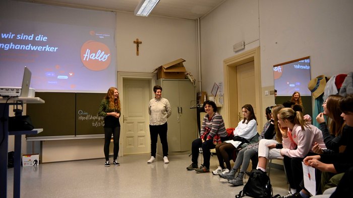 Jugendliche entdecken Berufe im Handwerk und Gastgewerbe Gruppe von Menschen in einem Klassenzimmer hört Vortrag vor einer Leinwand