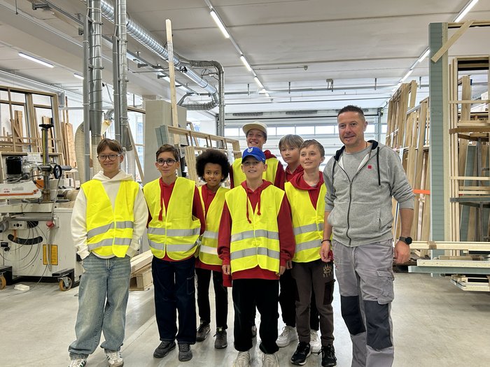 Eintauchen in die Welt der Berufe in Mühlbach Gruppe von Kindern mit gelben Sicherheitswesten in einer Werkstatt mit einem Erwachsenen