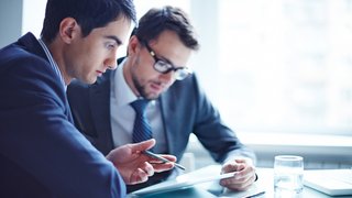 News Zwei Männer im Anzug diskutieren über ein Tablet in einem Büro