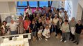 Frauenpower on Tour: Sommerausflug der „Frauen im Handwerk“ ins Fleimstal Große Gruppe von Frauen und Männern, die in einem Raum mit großen Fenstern posieren