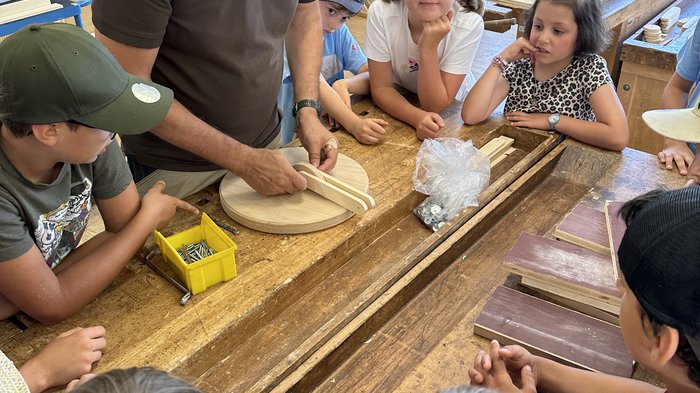 Kids-Academy 2024: buntes Handwerk in Bruneck Lehrer zeigt Kindern Holzarbeit in einer Werkstatt