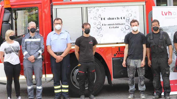 Riscaldare in modo indipendente e sicuro Persone con mascherine davanti a un camion dei pompieri rosso con numero di emergenza 112
