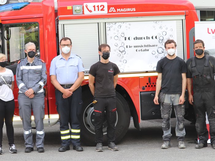 Unabhängige sichere Wärme Menschen mit Masken stehen vor einem roten Feuerwehrauto mit 112-Notrufnummer