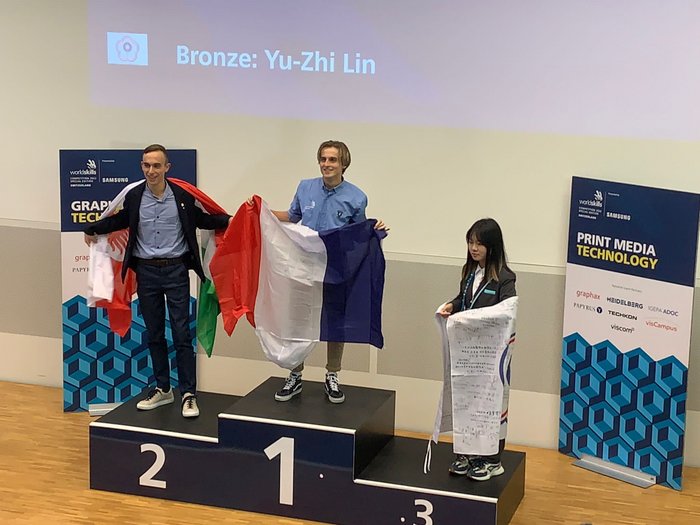 WorldSkills 2022 Special Edition: Weitere Silbermedaille für Südtirol Siegerpodium mit drei Personen, die Flaggen nach einer Grafiktechnologie-Meisterschaft halten.