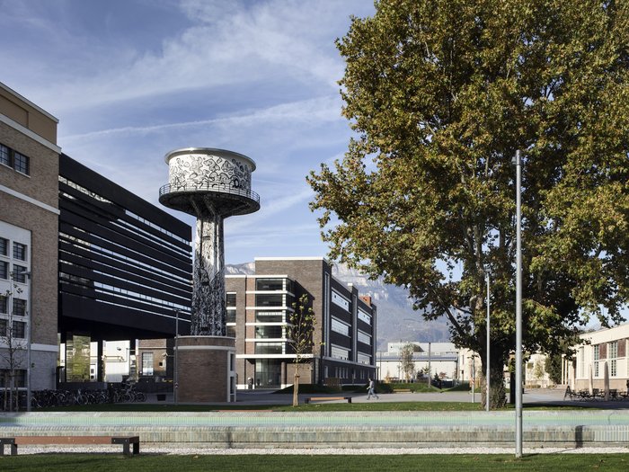 Avviata la procedura a evidenza pubblica per l’insediamento di imprese attraverso l’edificazione privata al NOI Techpark di Bol-zano Vista urbana con torre d'acqua decorata e edifici moderni sotto un cielo limpido